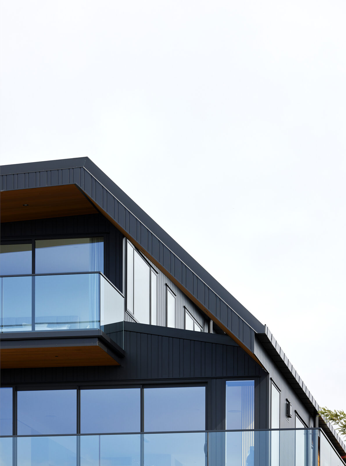 Close-up of the black cladding and angled roofline against the sky, with a cedar-lined balcony soffit below
