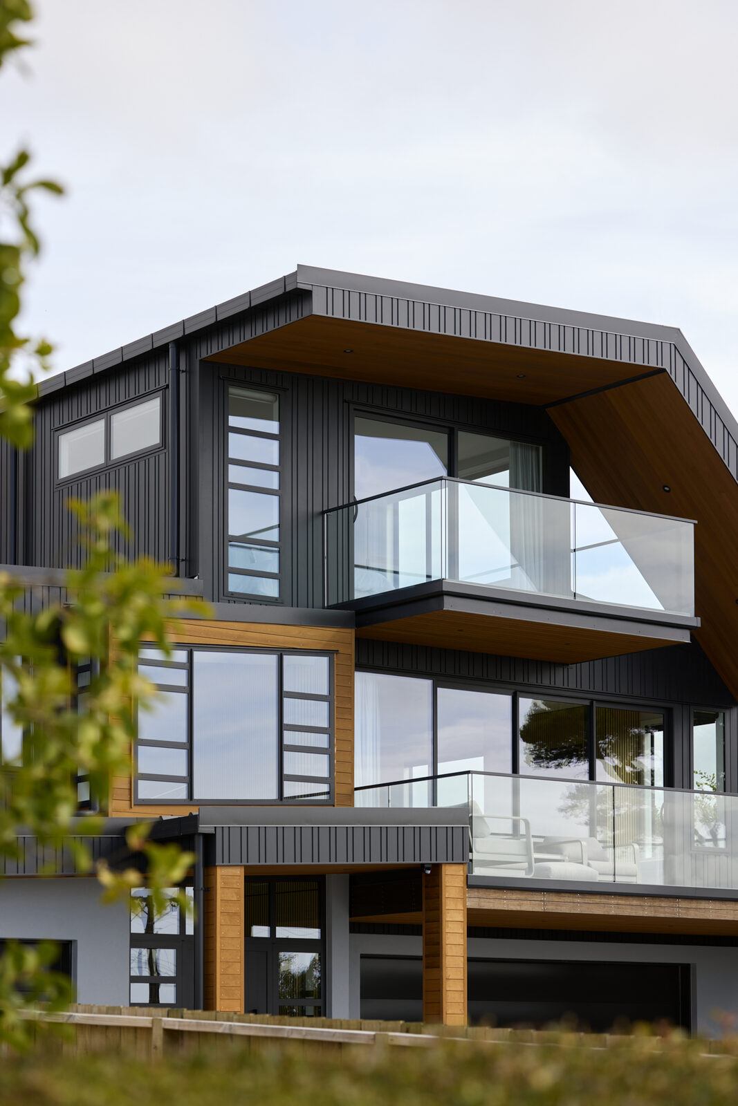 Close-up of the home's dark cladding and stacked glass balconies, seen through foreground foliage