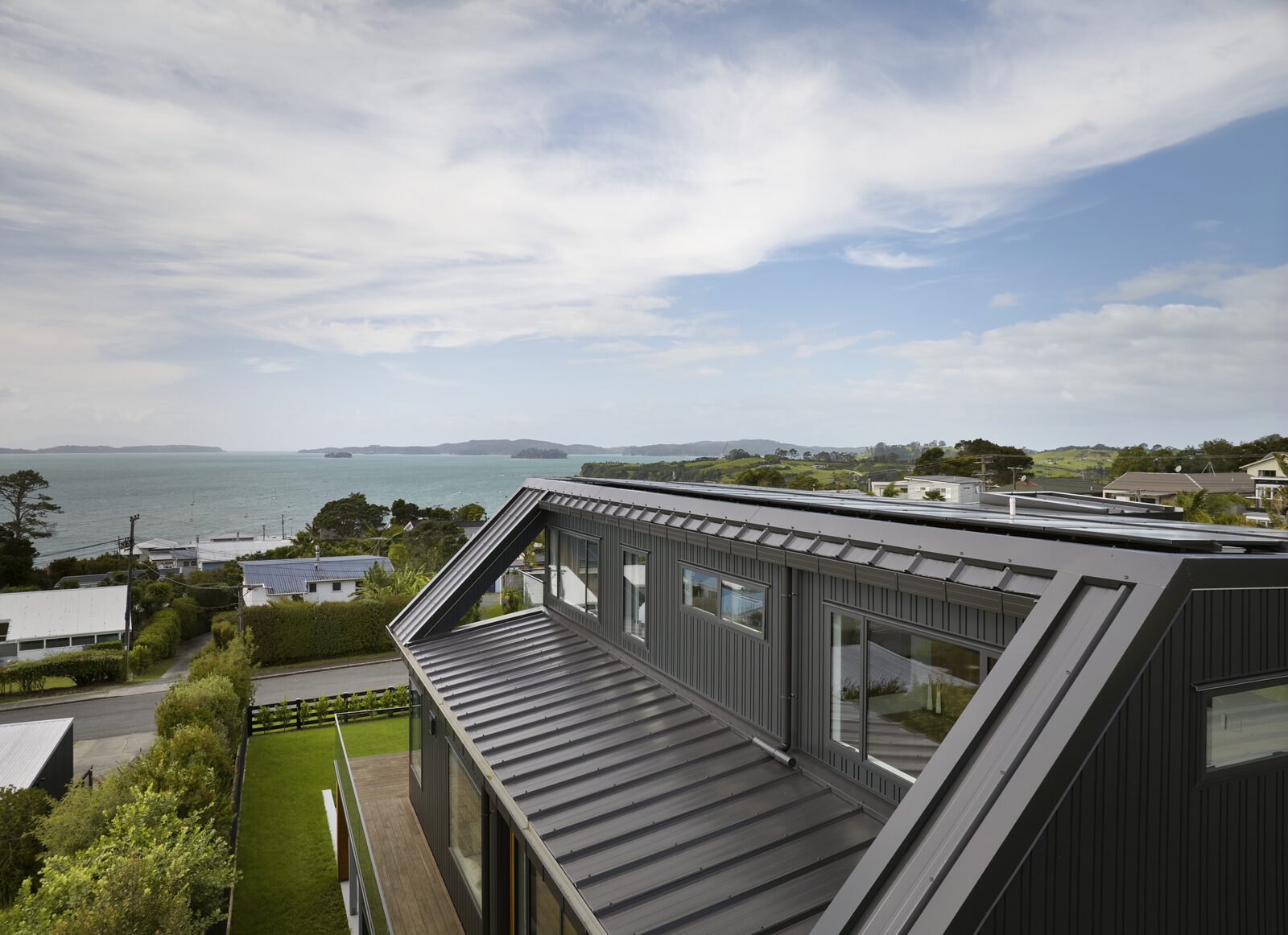 Aerial view along the standing-seam roofline toward the Hauraki Gulf coastline