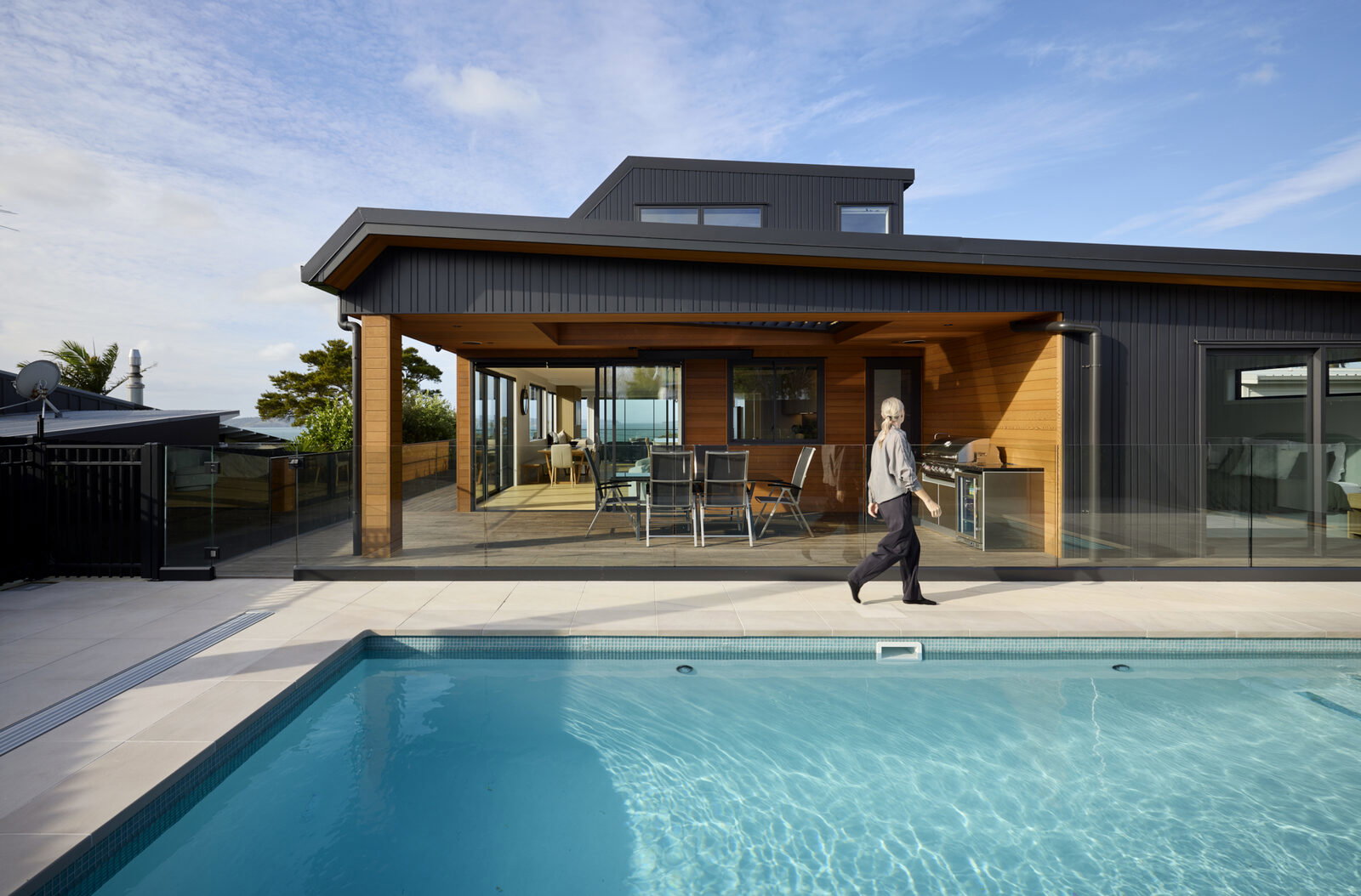 Covered timber-lined alfresco deck with outdoor dining and kitchen, opening onto the pool