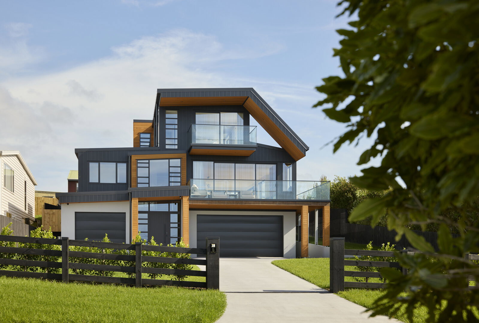 Street-facing exterior with twin garages, cedar entry porch and dark timber picket fencing